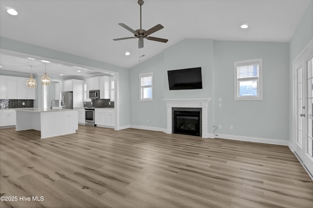 unfurnished living room with baseboards, light wood-style flooring, a fireplace, and vaulted ceiling