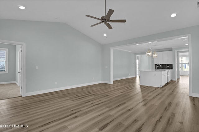 unfurnished living room featuring a ceiling fan, a sink, light wood-style floors, baseboards, and vaulted ceiling