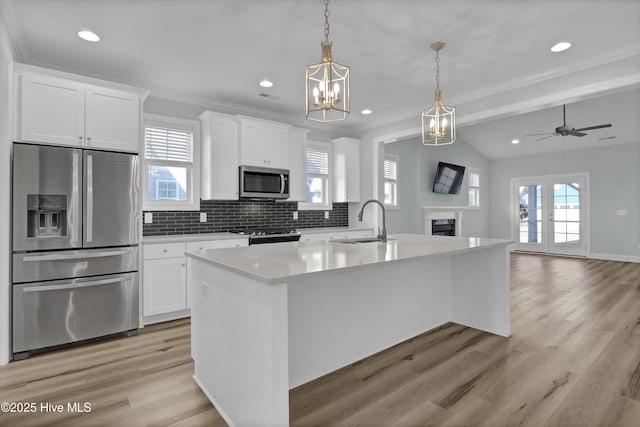 kitchen with tasteful backsplash, an island with sink, white cabinets, stainless steel appliances, and a sink