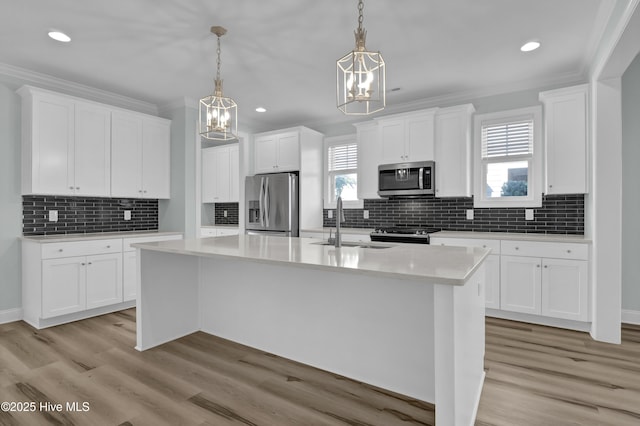 kitchen with light wood-style flooring, a kitchen island with sink, light countertops, appliances with stainless steel finishes, and crown molding