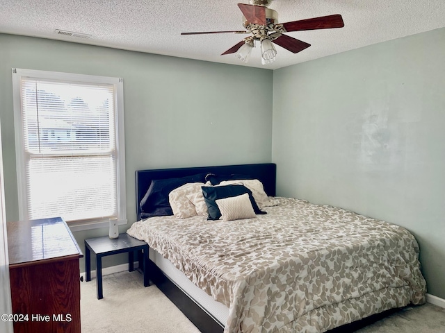 bedroom with ceiling fan, light colored carpet, and a textured ceiling