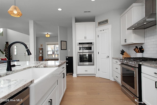 kitchen featuring sink, light hardwood / wood-style flooring, wall chimney exhaust hood, appliances with stainless steel finishes, and white cabinetry