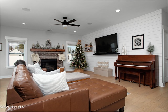 living room featuring ceiling fan, light wood-type flooring, and a brick fireplace