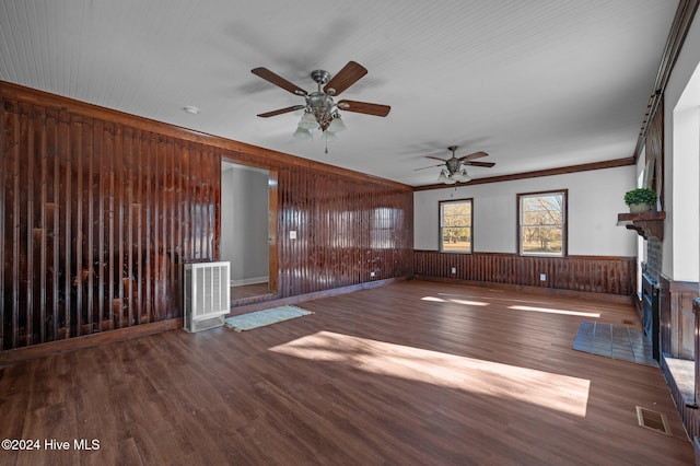 unfurnished living room with ceiling fan, crown molding, dark wood-type flooring, and wooden walls