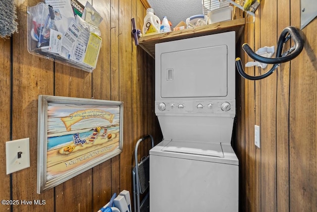 laundry area featuring stacked washer and clothes dryer, a textured ceiling, and wood walls