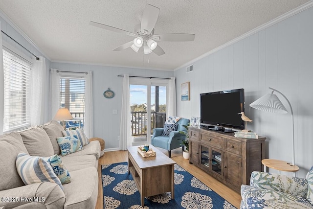 living room featuring ceiling fan, ornamental molding, light hardwood / wood-style floors, and a textured ceiling