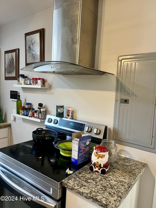 kitchen with electric range, wall chimney exhaust hood, stone countertops, and electric panel