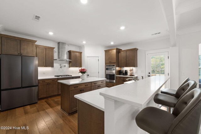 kitchen with a breakfast bar, wall chimney range hood, a kitchen island, decorative backsplash, and stainless steel appliances