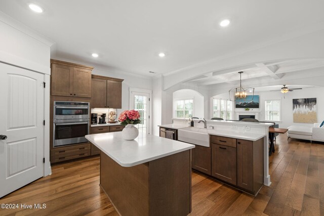 kitchen featuring sink, coffered ceiling, a center island with sink, and beamed ceiling