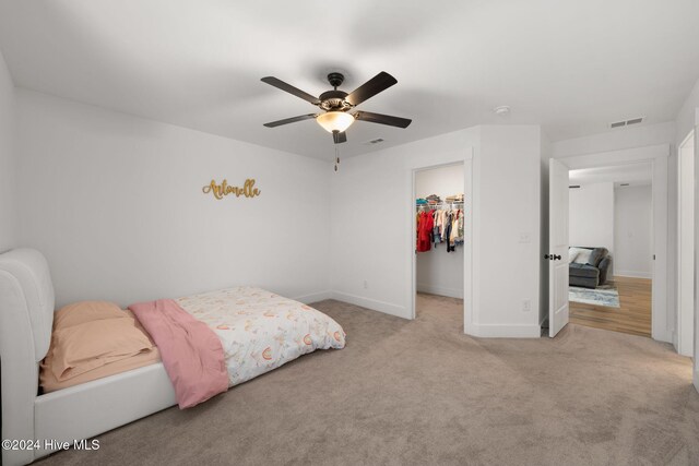 bedroom featuring a spacious closet, a closet, light carpet, and ceiling fan