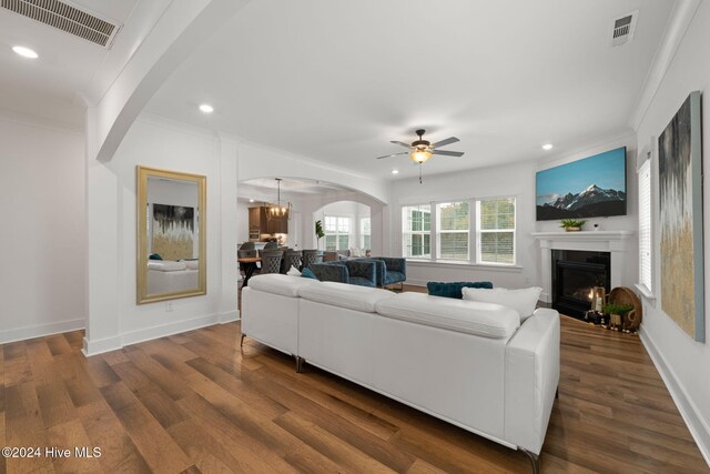 living room with ceiling fan with notable chandelier, dark hardwood / wood-style floors, and crown molding