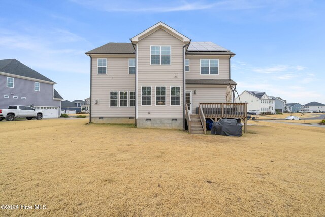 rear view of house featuring a deck, a yard, and solar panels