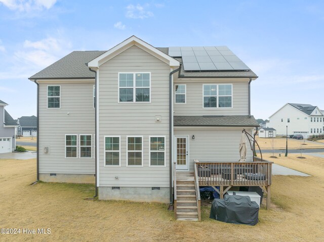 rear view of property with a wooden deck, a lawn, and solar panels