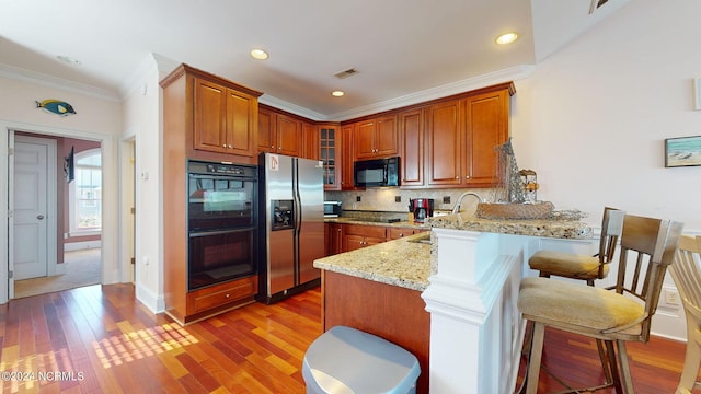 kitchen with backsplash, black appliances, a kitchen breakfast bar, light hardwood / wood-style floors, and kitchen peninsula