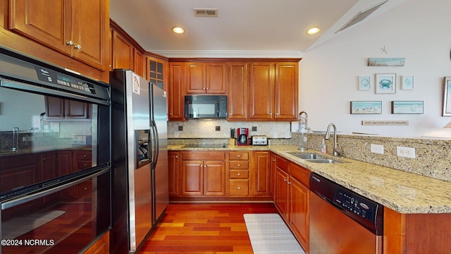 kitchen featuring backsplash, black appliances, sink, light hardwood / wood-style floors, and light stone counters