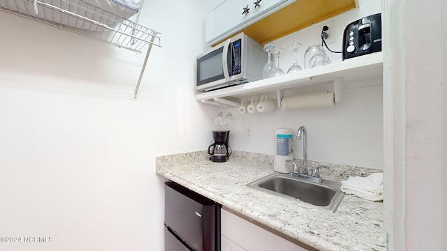 kitchen with light stone countertops, white cabinetry, and sink