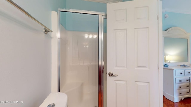 bathroom with wood-type flooring, a shower with shower door, and crown molding