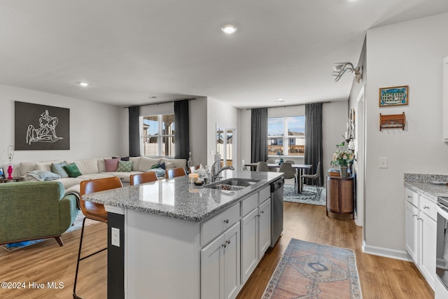 kitchen with stainless steel dishwasher, light wood-style flooring, light stone counters, and a sink