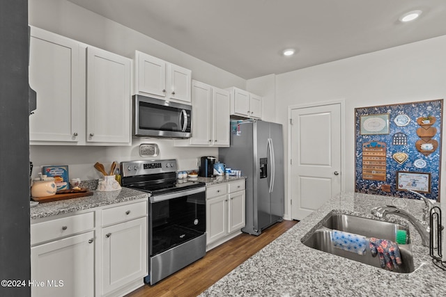 kitchen featuring wood finished floors, appliances with stainless steel finishes, white cabinetry, a sink, and light stone countertops