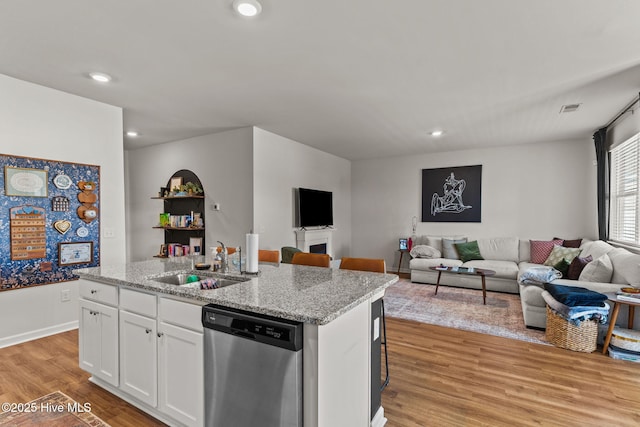 kitchen featuring white cabinets, open floor plan, light wood-type flooring, stainless steel dishwasher, and a sink