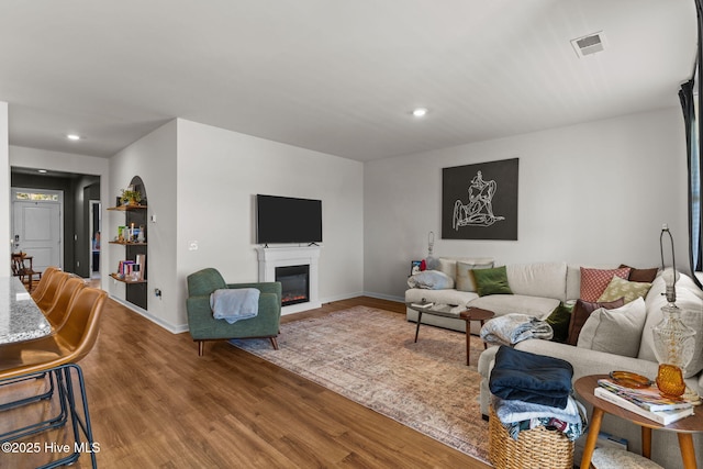 living area with recessed lighting, wood finished floors, visible vents, baseboards, and a glass covered fireplace