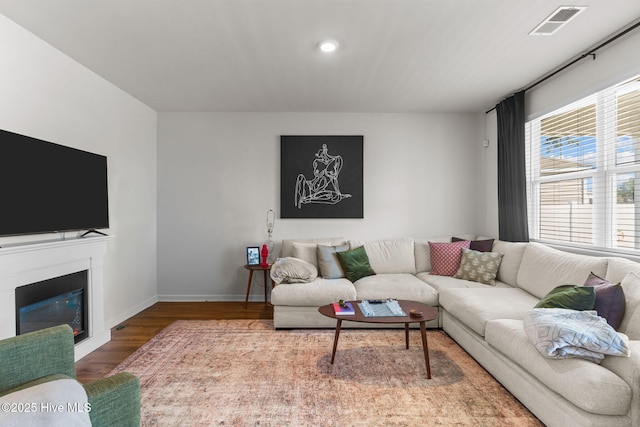 living room with a glass covered fireplace, wood finished floors, visible vents, and baseboards