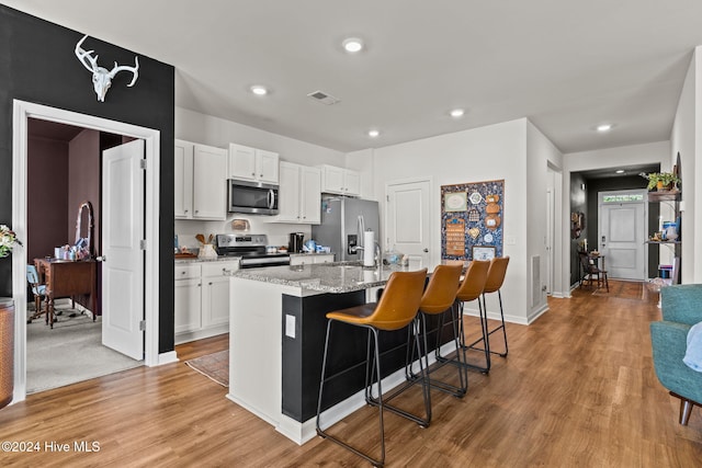 kitchen with stainless steel appliances, visible vents, light wood-style floors, white cabinets, and a center island with sink