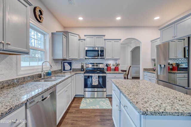 kitchen with light stone countertops, appliances with stainless steel finishes, dark hardwood / wood-style flooring, sink, and a kitchen island