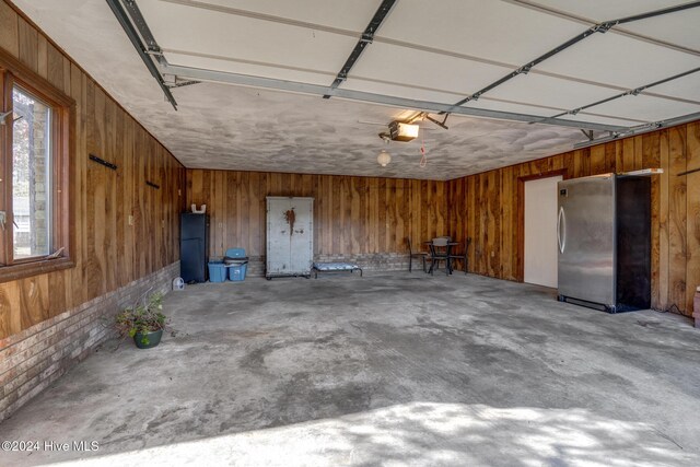 garage with wood walls, a garage door opener, and stainless steel refrigerator