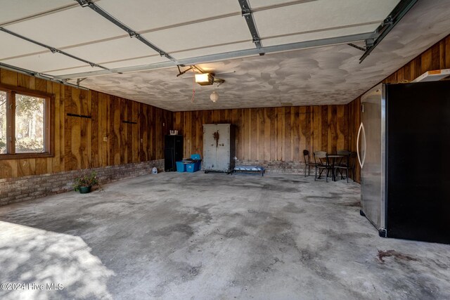 garage with stainless steel fridge, a garage door opener, and wood walls