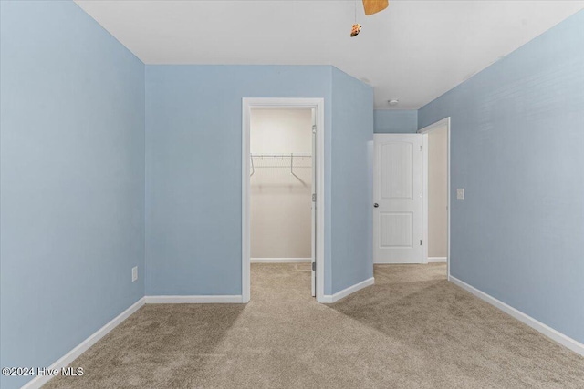 unfurnished bedroom featuring a walk in closet, light colored carpet, a closet, and ceiling fan