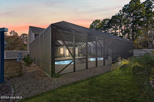 pool at dusk featuring a yard and glass enclosure