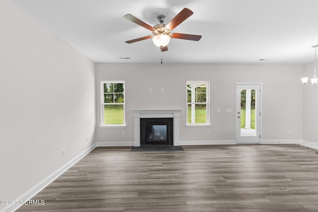 unfurnished living room with ceiling fan with notable chandelier and dark wood-type flooring