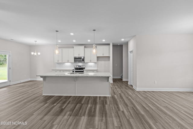 kitchen with white cabinetry, light stone countertops, stainless steel appliances, hardwood / wood-style floors, and a kitchen island with sink