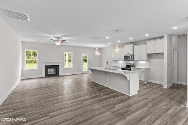 kitchen featuring light stone countertops, appliances with stainless steel finishes, a kitchen island with sink, white cabinets, and hanging light fixtures