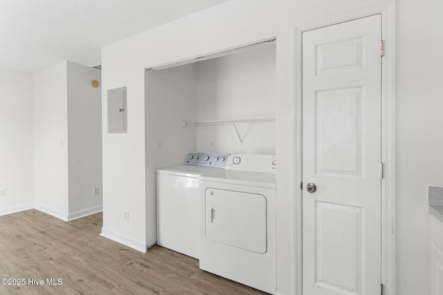 laundry room featuring electric panel, washing machine and clothes dryer, a textured ceiling, and light hardwood / wood-style flooring