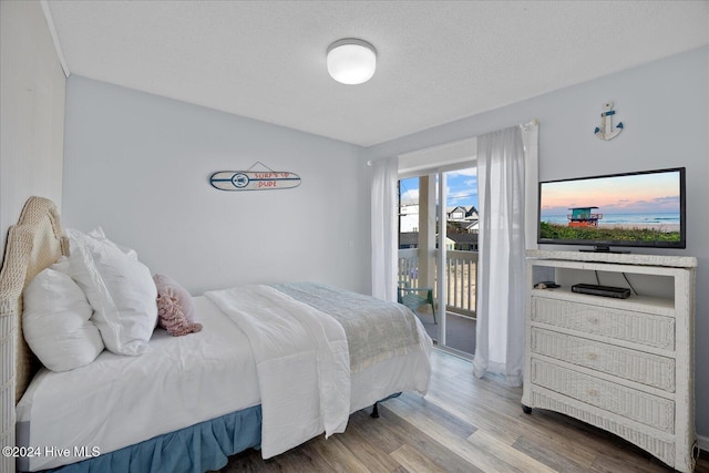 bedroom with access to exterior, wood-type flooring, and a textured ceiling