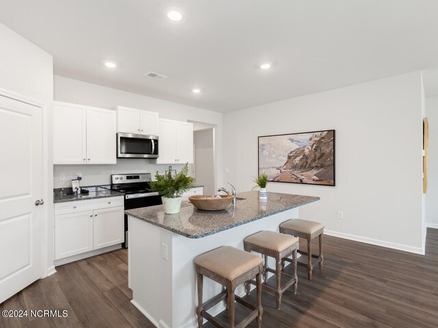 kitchen with white cabinets, dark wood-type flooring, stainless steel appliances, and an island with sink