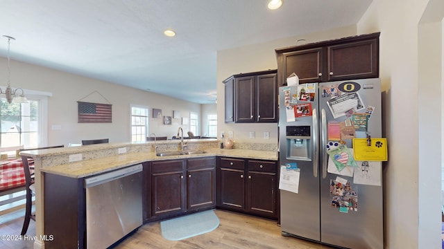 kitchen with light stone counters, a peninsula, a sink, stainless steel appliances, and dark brown cabinets