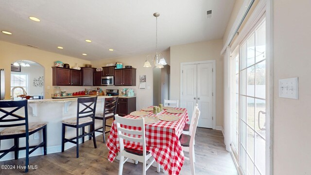 dining space with a wealth of natural light, arched walkways, light wood-style floors, and recessed lighting