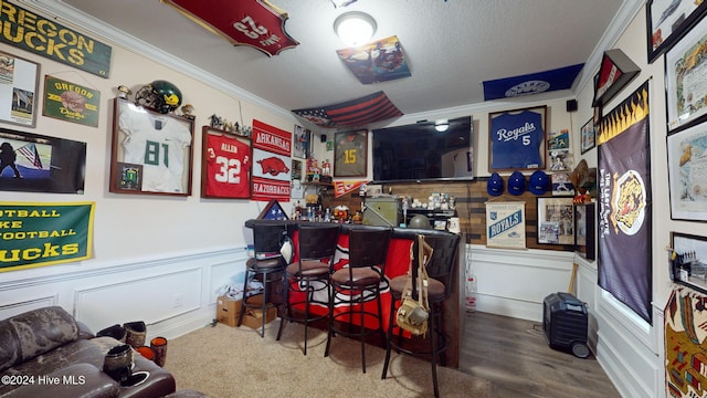 recreation room with ornamental molding, wood finished floors, a bar, wainscoting, and a decorative wall