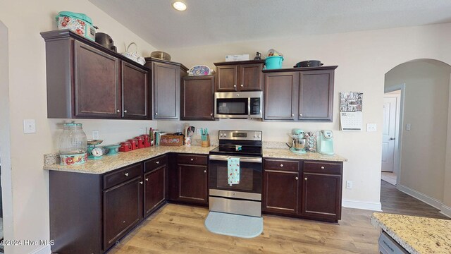 kitchen with light wood finished floors, dark brown cabinets, appliances with stainless steel finishes, arched walkways, and a sink