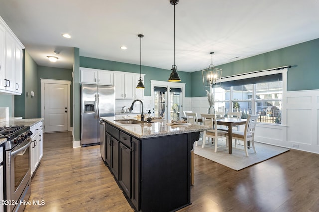 kitchen featuring light stone countertops, stainless steel appliances, sink, hanging light fixtures, and an island with sink