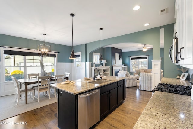 kitchen featuring ceiling fan with notable chandelier, sink, light stone countertops, an island with sink, and appliances with stainless steel finishes