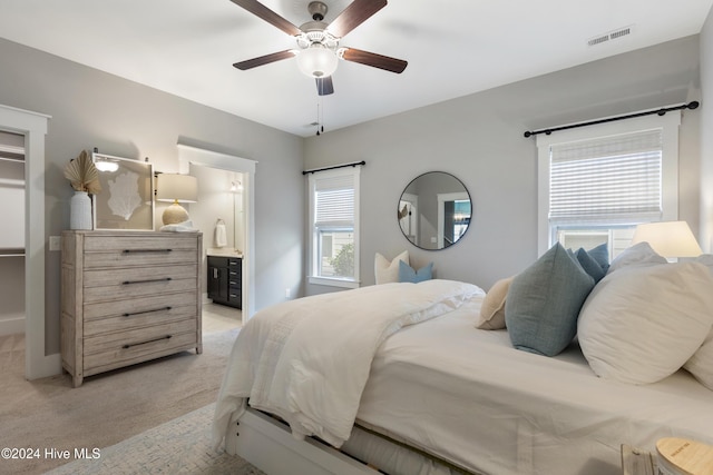 carpeted bedroom with ceiling fan, multiple windows, and ensuite bath