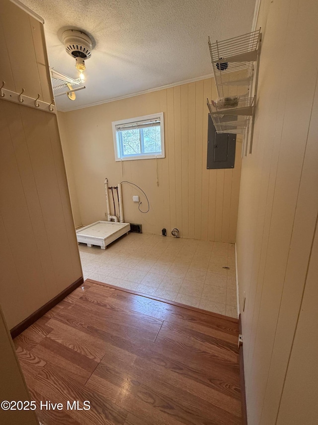 laundry room featuring wooden walls, wood finished floors, electric panel, a textured ceiling, and crown molding