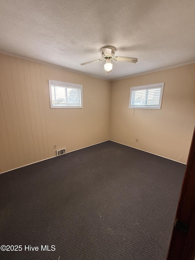 empty room featuring dark colored carpet, visible vents, and a textured ceiling