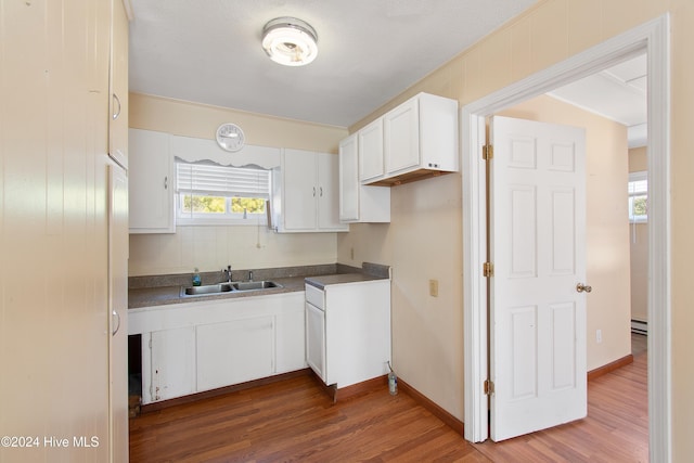 kitchen with a sink, dark countertops, wood finished floors, and white cabinetry