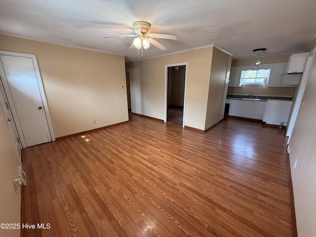 unfurnished living room with a sink, wood finished floors, ceiling fan, and ornamental molding