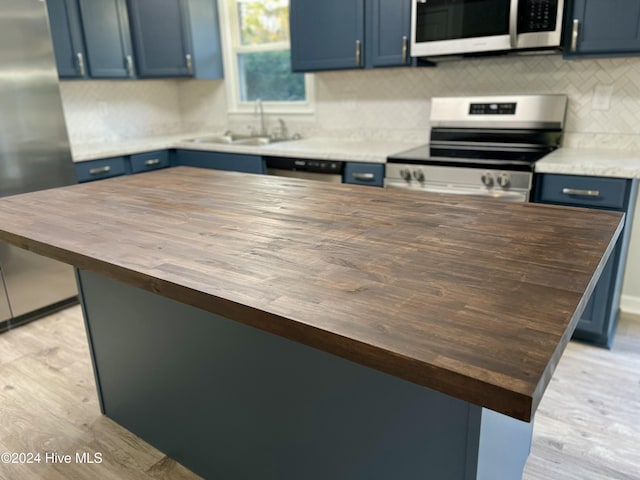 kitchen with sink, blue cabinets, butcher block countertops, appliances with stainless steel finishes, and light wood-type flooring